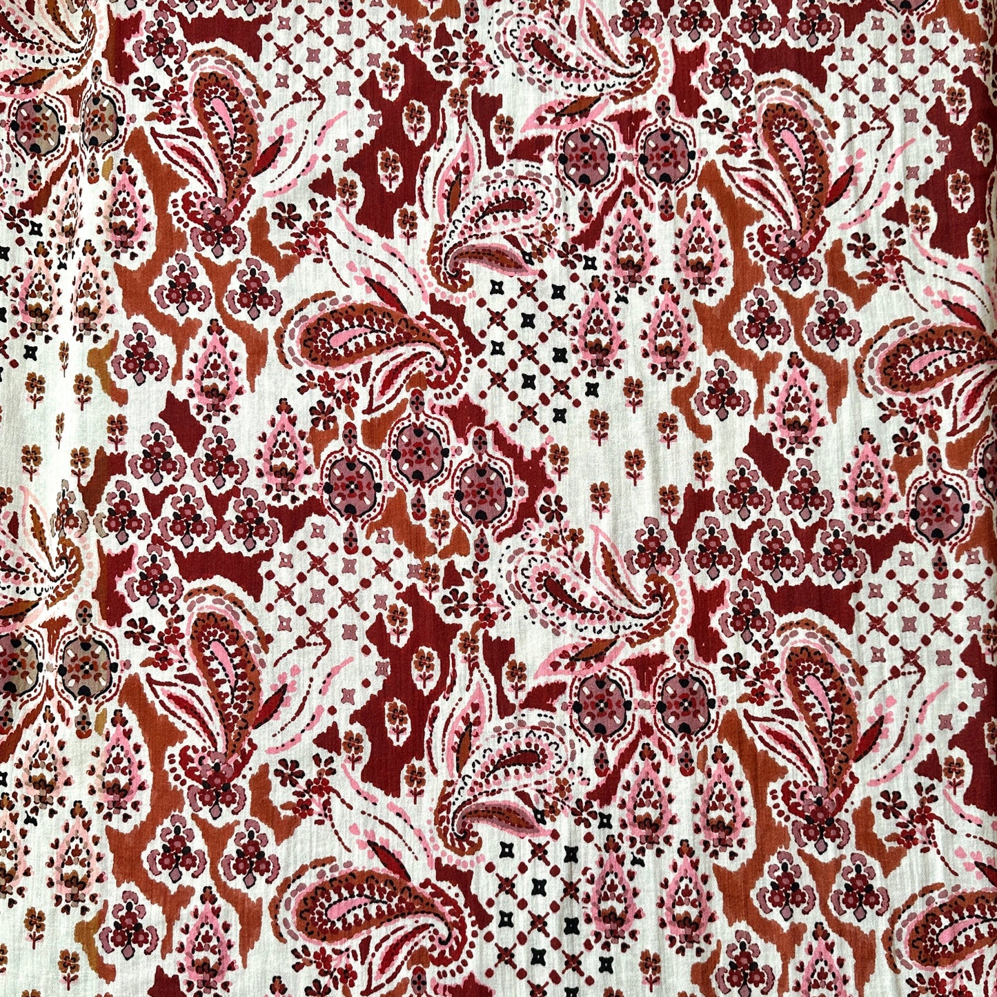 Dressmaking fabric with paisley design in browns, burgundy and pinks on a cream background.