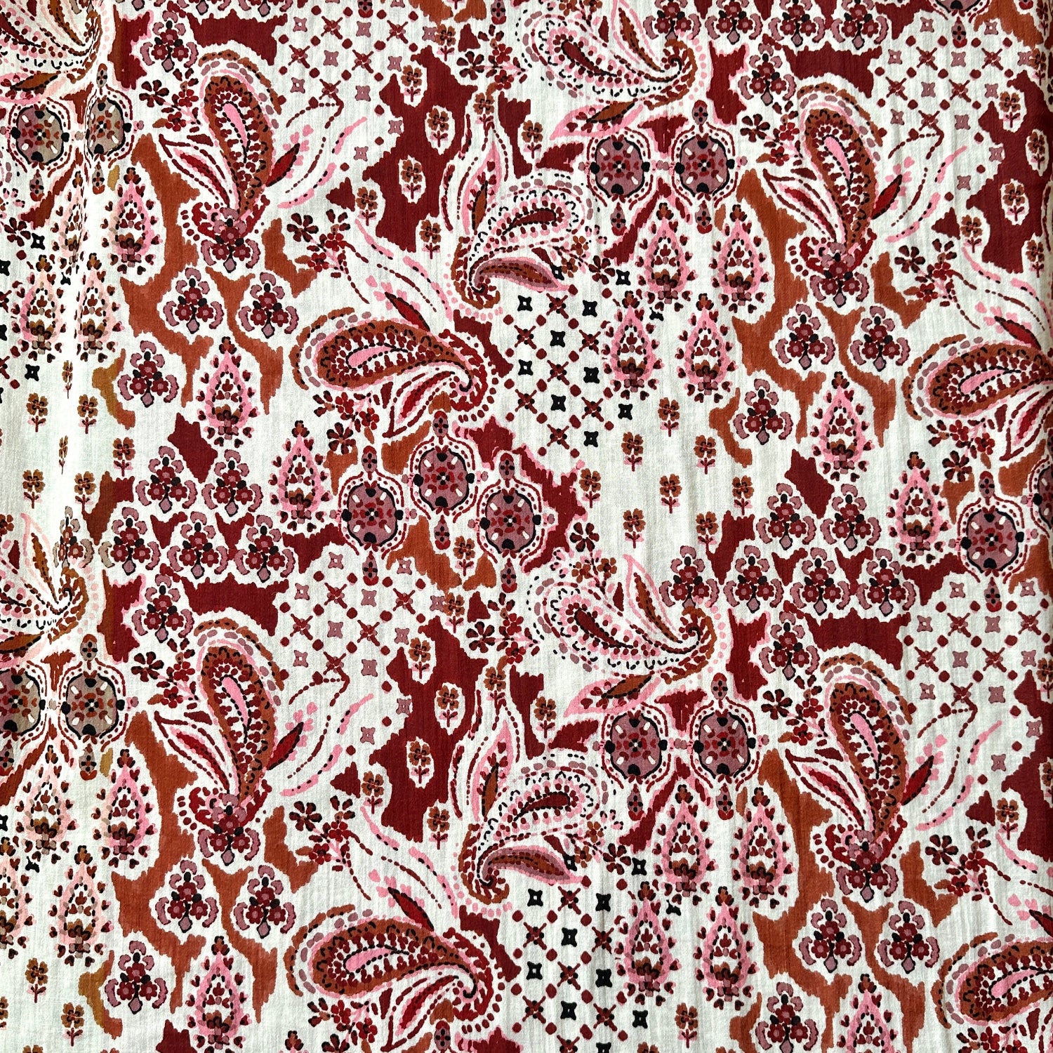 Dressmaking fabric with paisley design in browns, burgundy and pinks on a cream background.