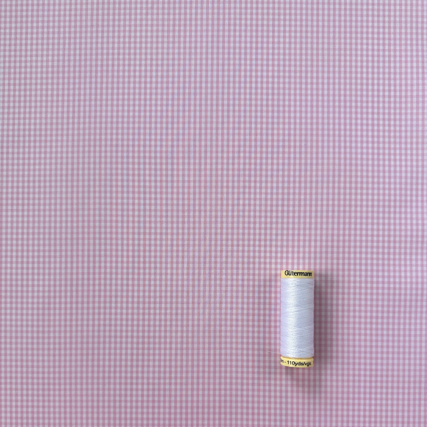 Spool of thread on a pink and white gingham fabric