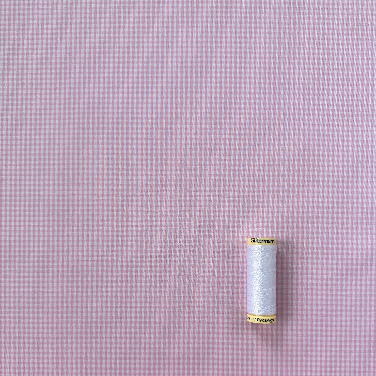 Spool of thread on a pink and white gingham fabric