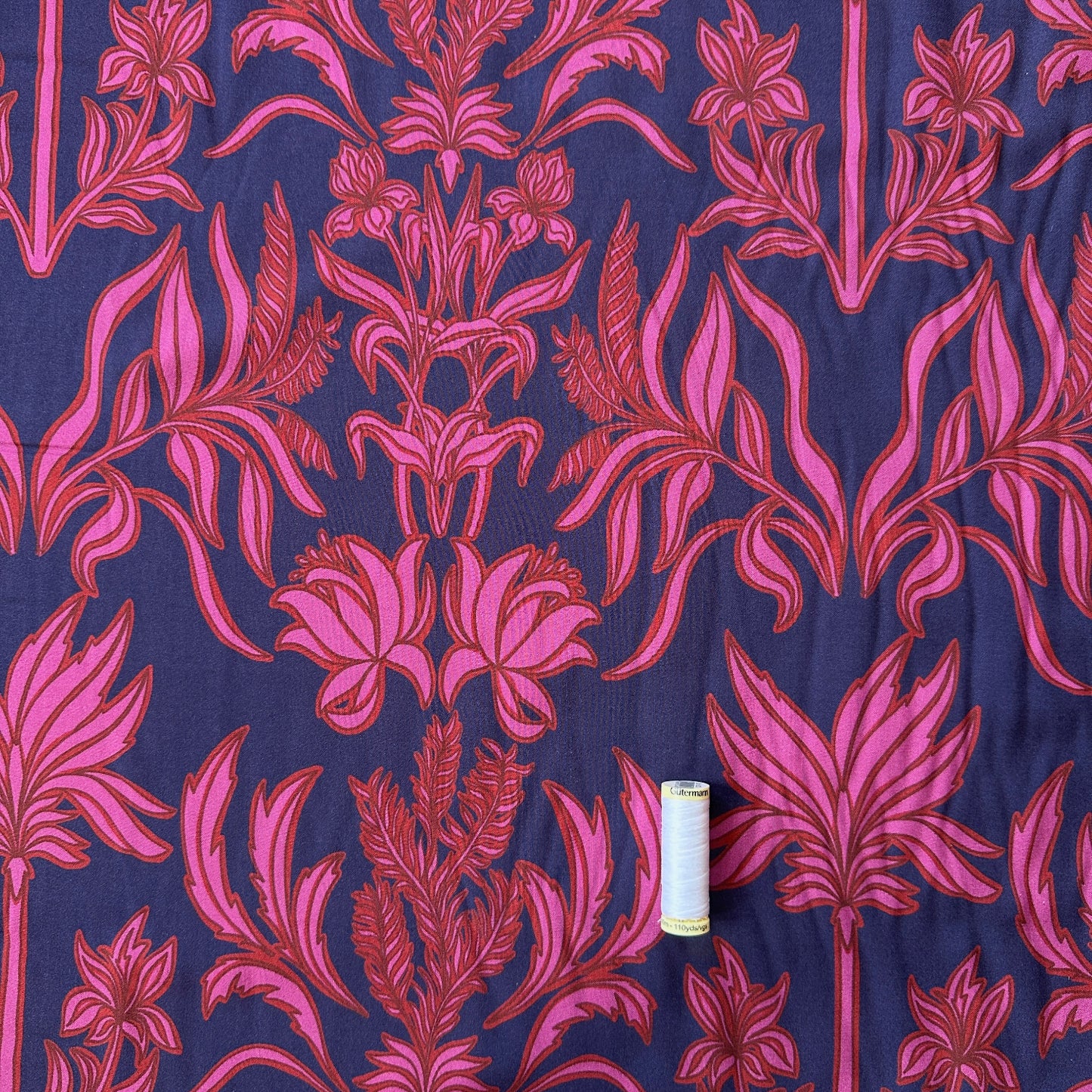 A navy fabric with floral design in pink and red and a reel of thread for scale