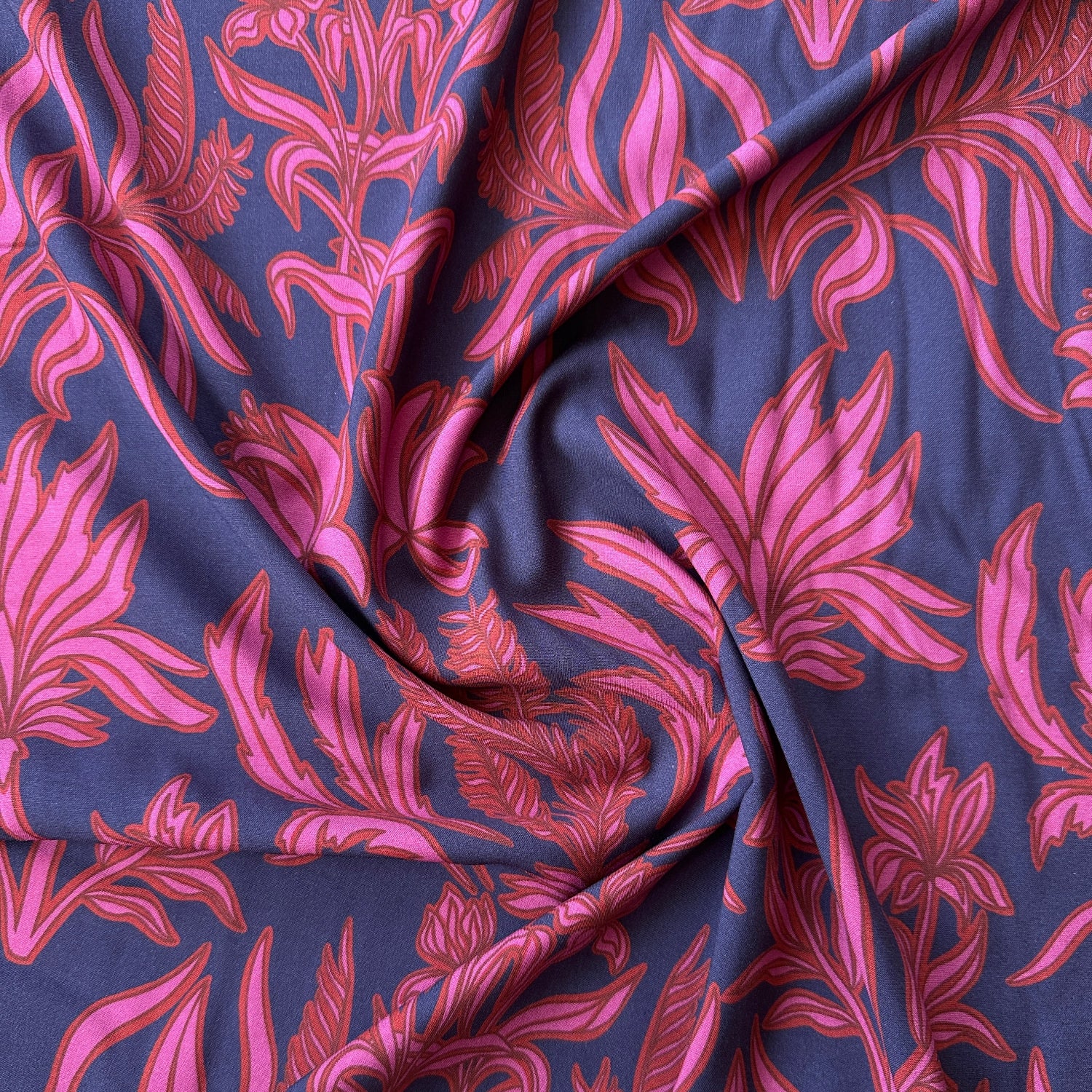 A swirl of viscose fabric in navy blue with pink and red flowers across it