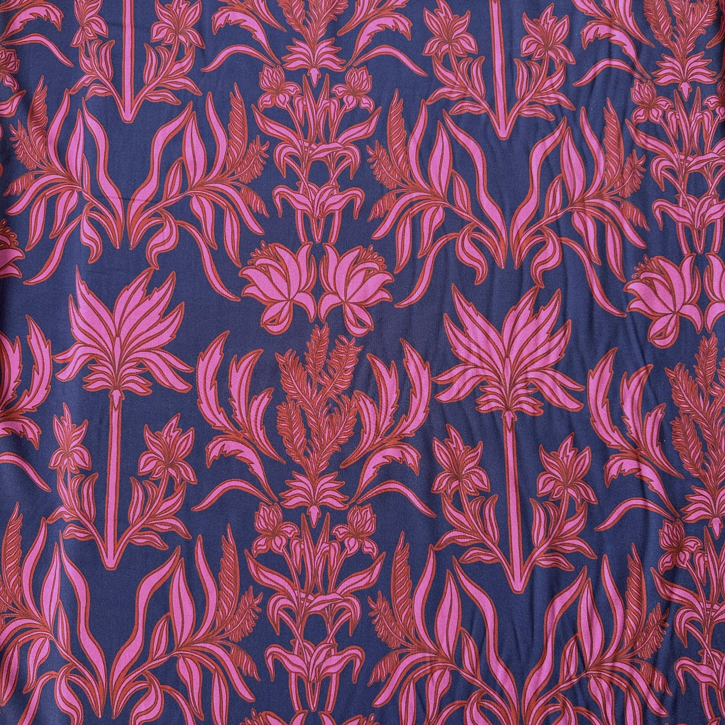 A close-up of a patterned fabric featuring a repeating botanical damask design in pink and red on a dark navy blue background.