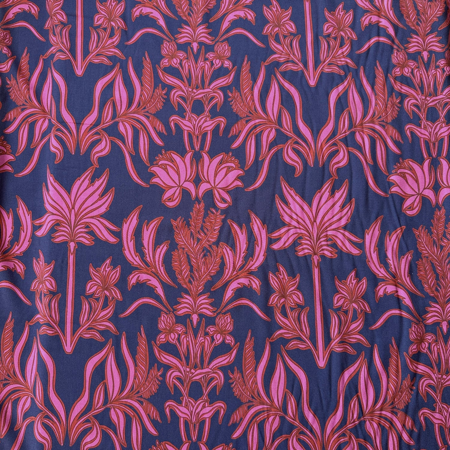 A close-up of a patterned fabric featuring a repeating botanical damask design in pink and red on a dark navy blue background.