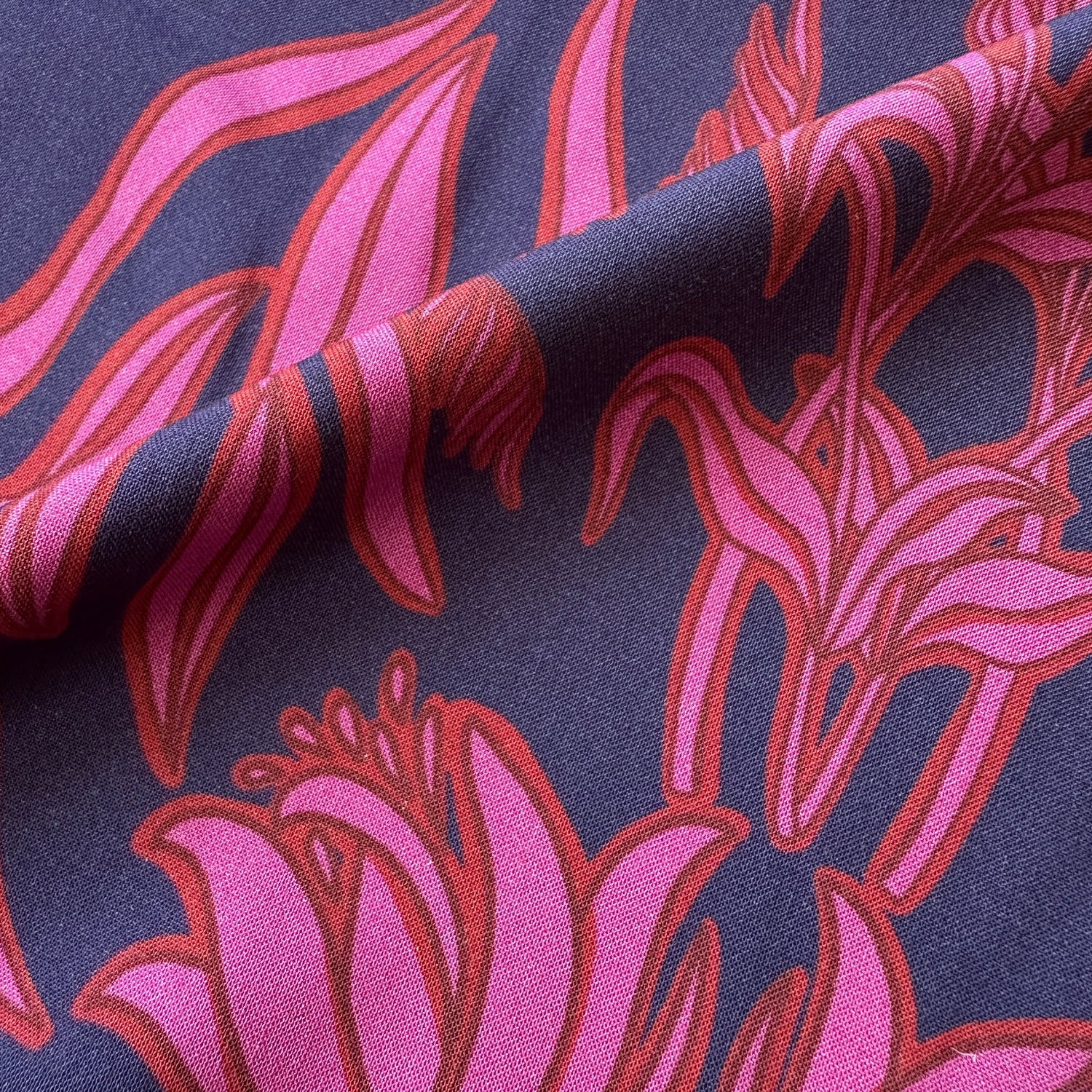 A close-up of patterned fabric with large pink floral motifs outlined in red on a dark navy background.