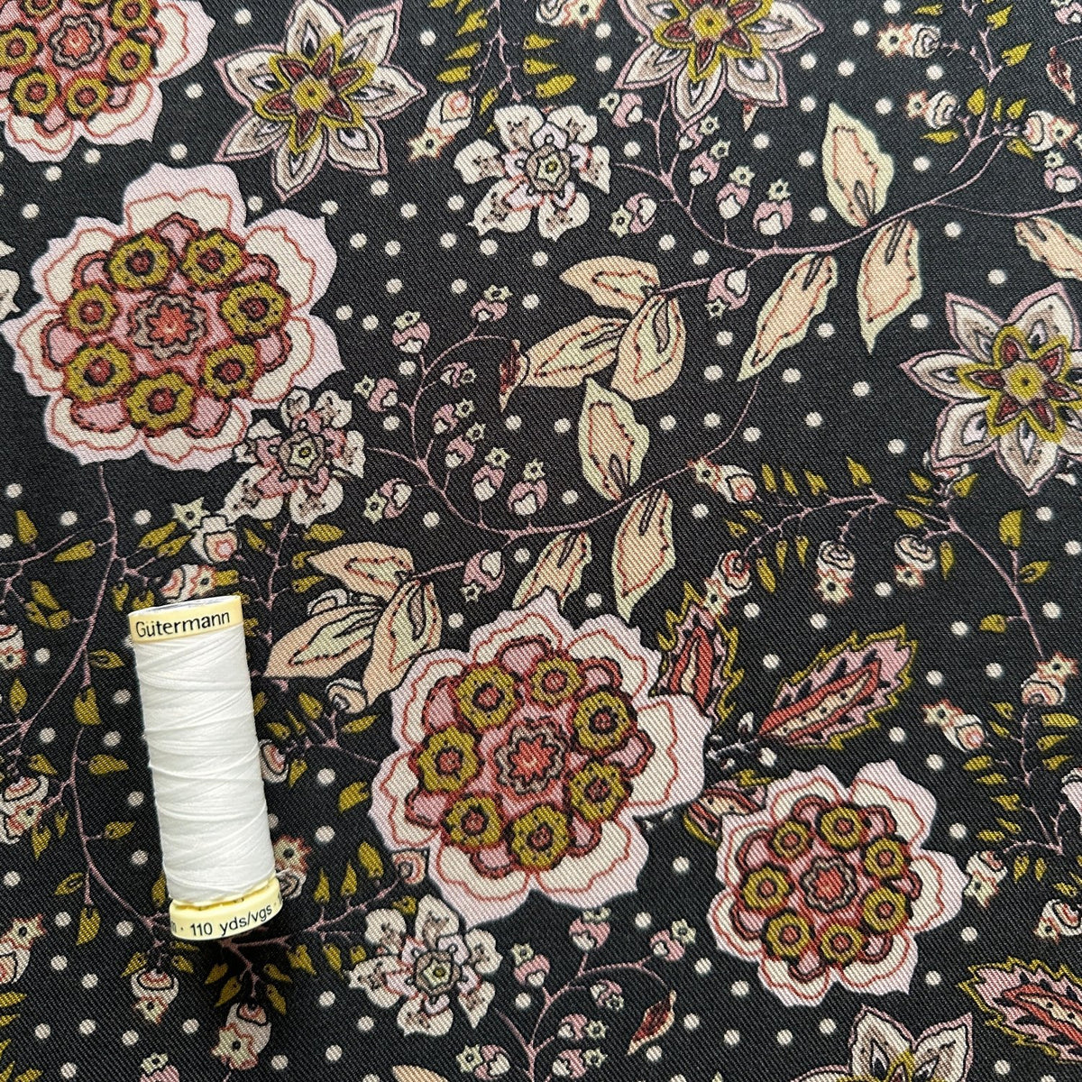 Reel of white thread showing scale of flowers on this floral viscose twill fabric