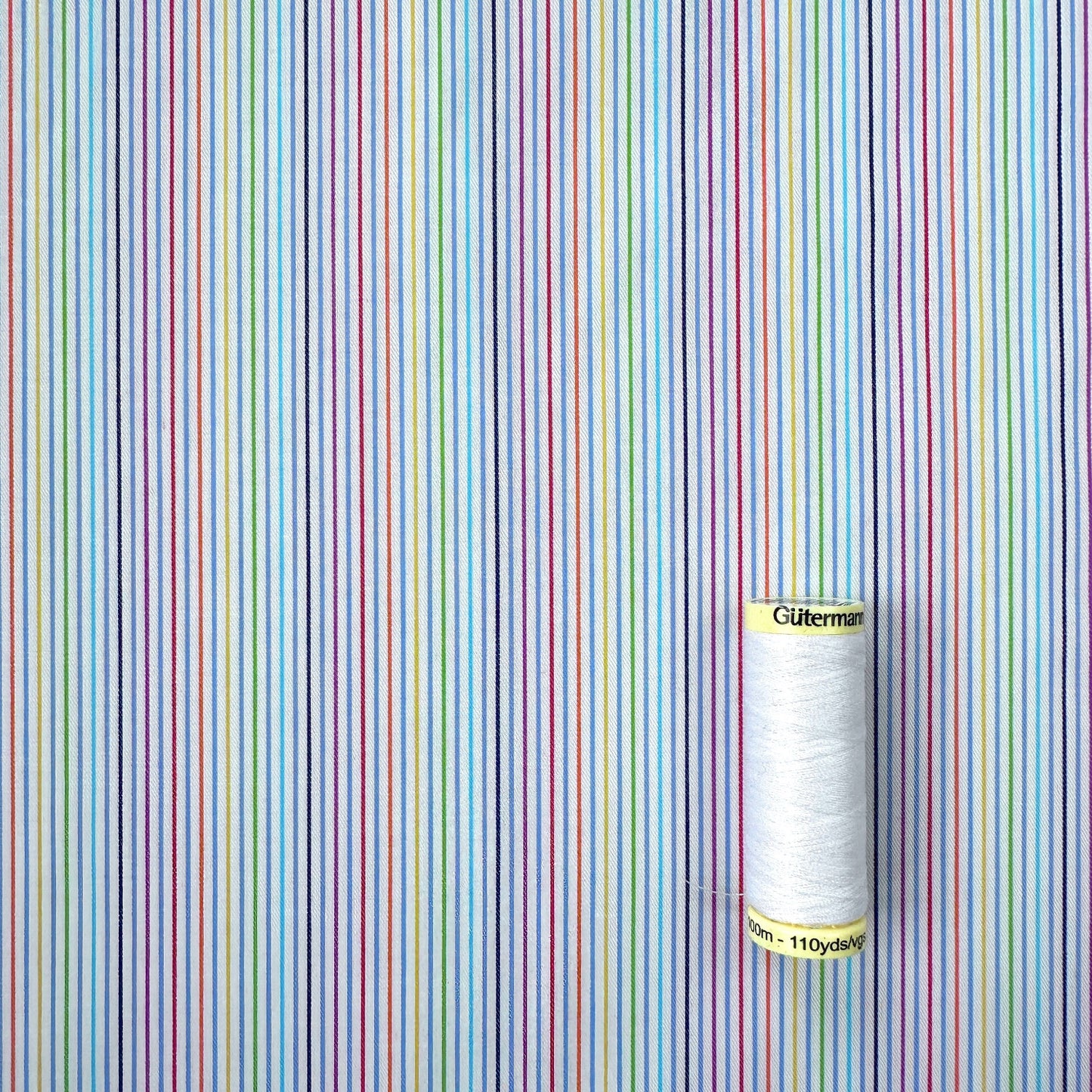 Reel of thread on a background with multicoloured vertical stripes