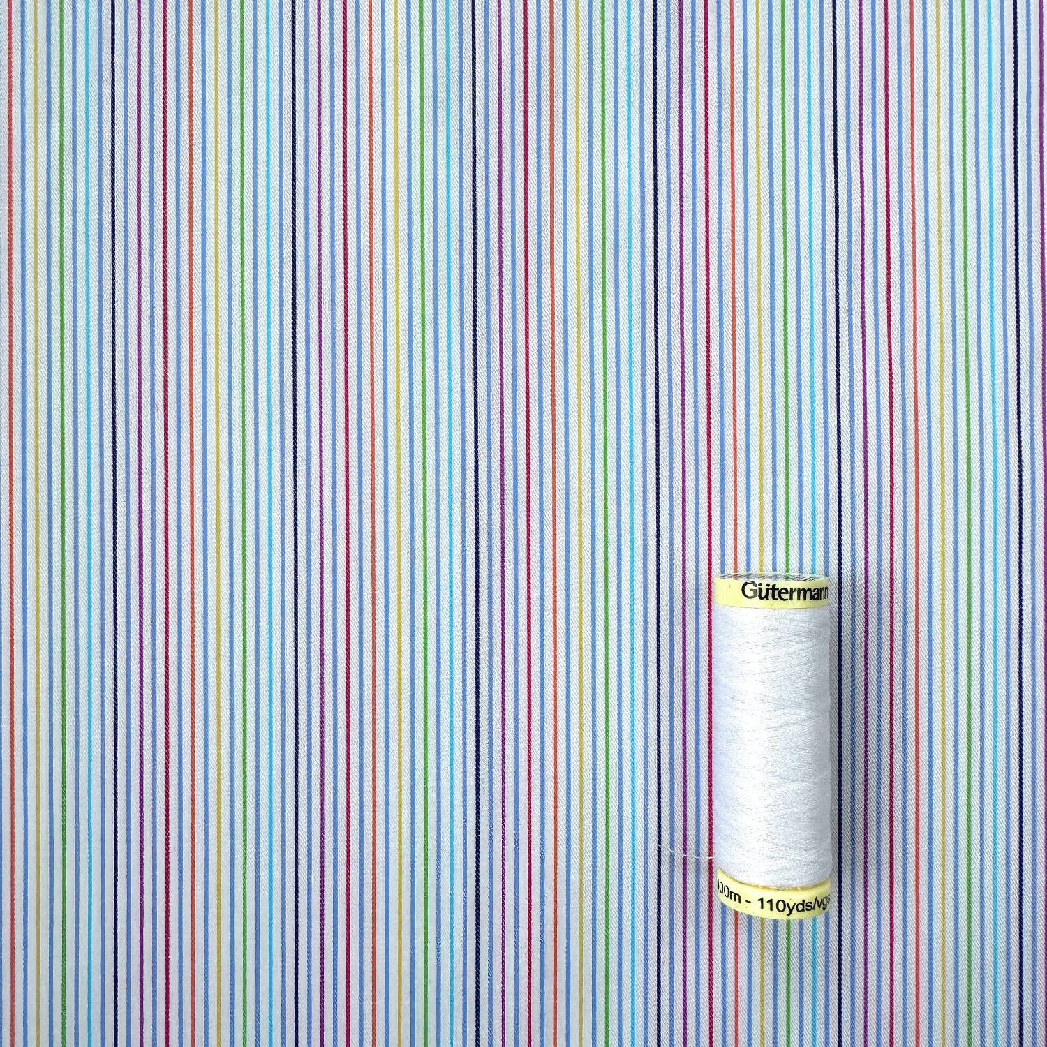 Reel of thread on a background with multicoloured vertical stripes