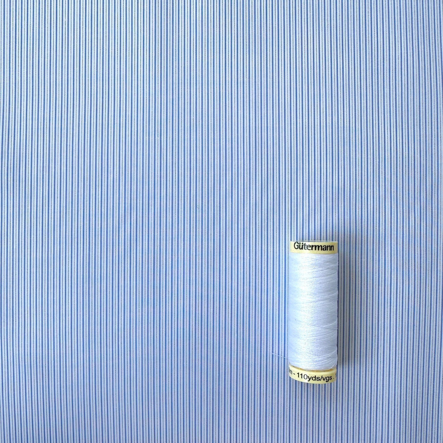 Reel of thread on blue and white stripe cotton fabric