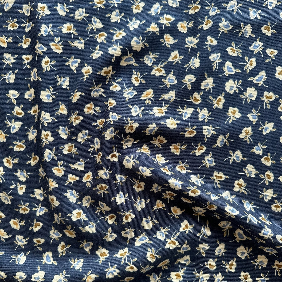 Folds of navy viscose twill dressmaking fabric with small flowers across it
