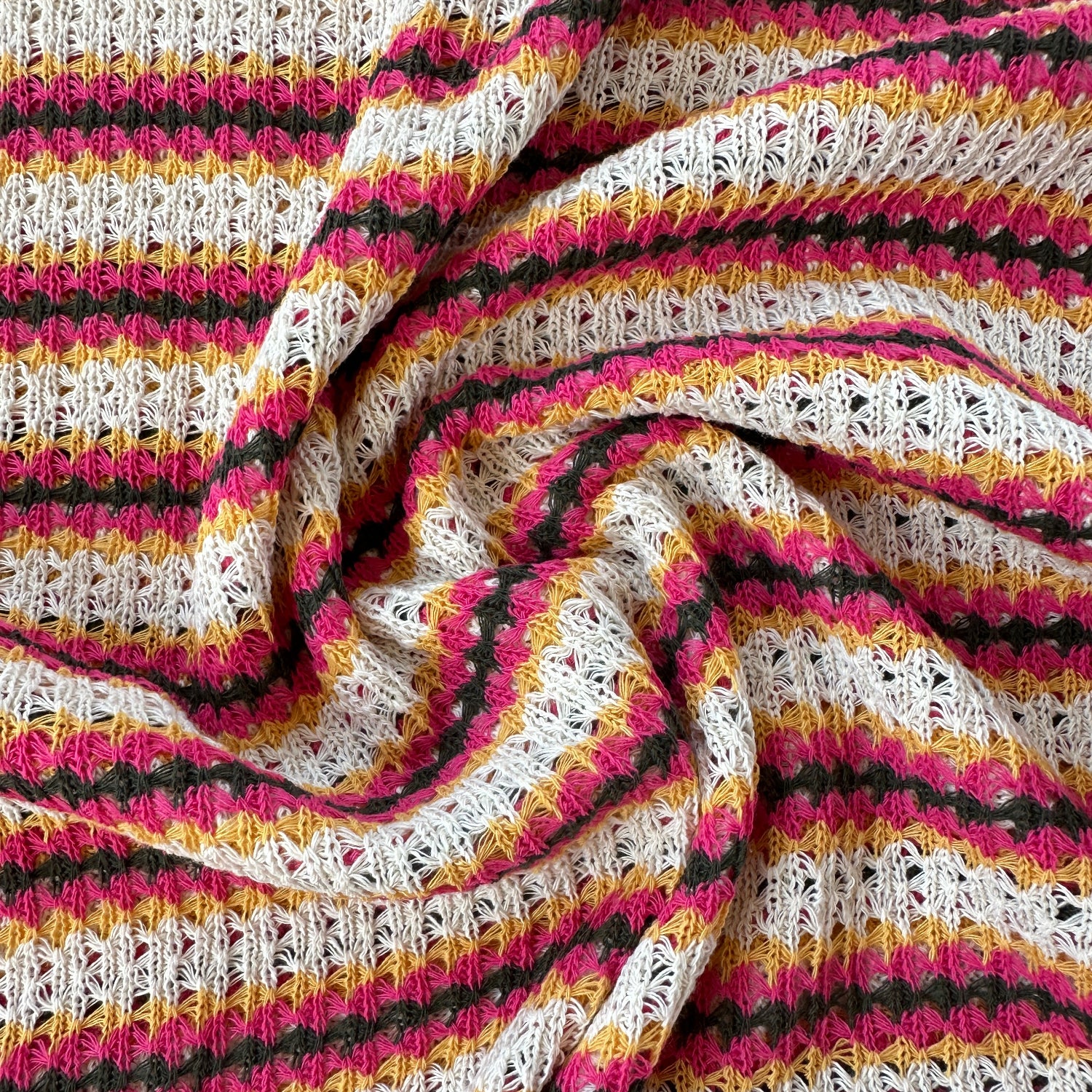 A close-up of a textured crochet fabric with vertical stripes in ecru, pink, yellow, and grey.