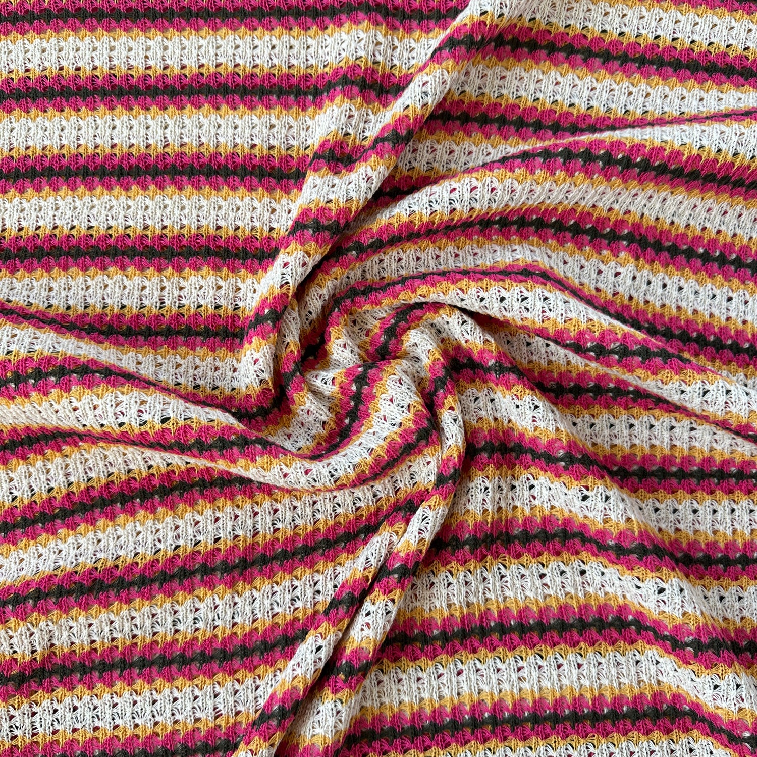 A close-up of a textured knit fabric with vertical stripes in ecru, pink, grey and yellow.