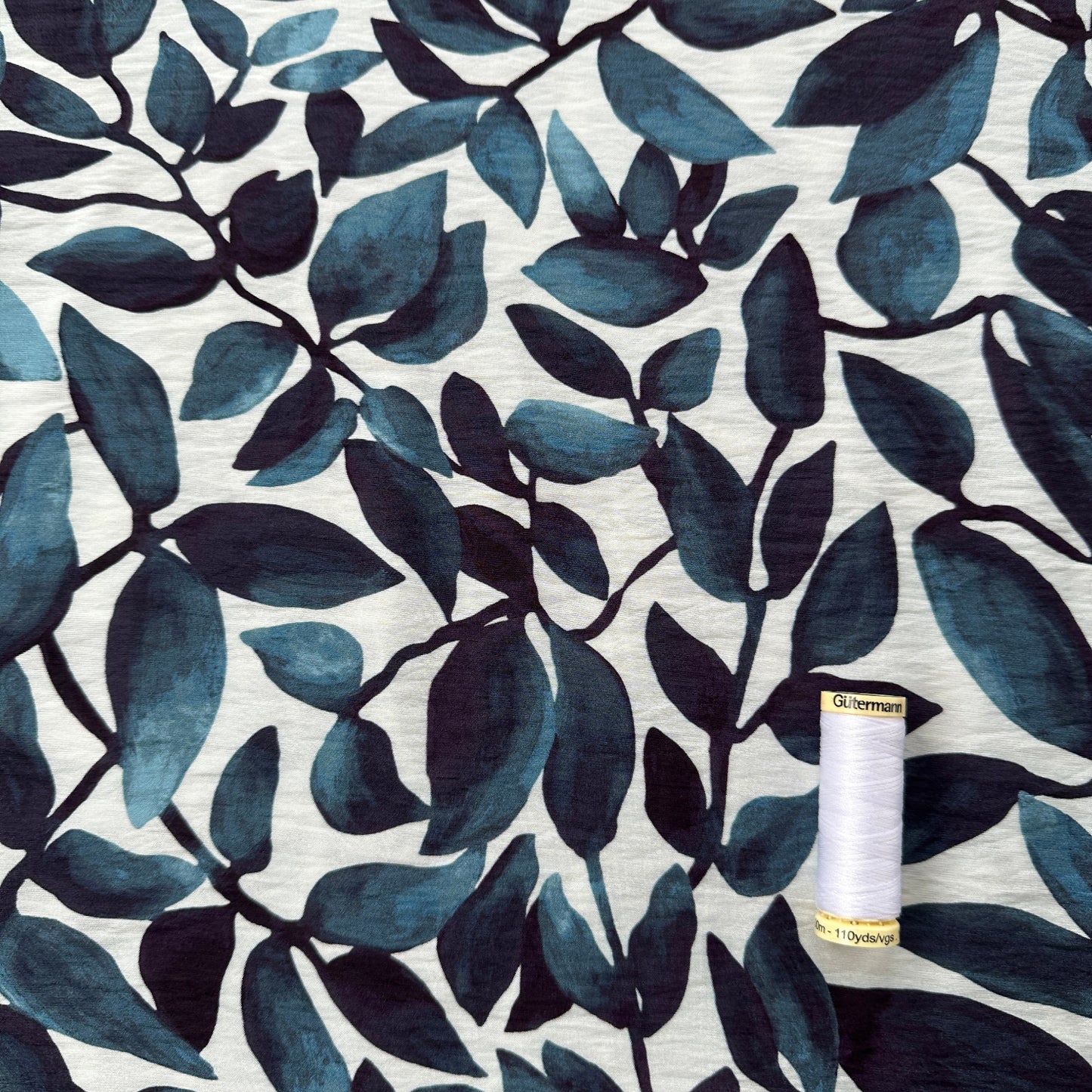Fabric with blue leaf pattern and a spool of thread on top