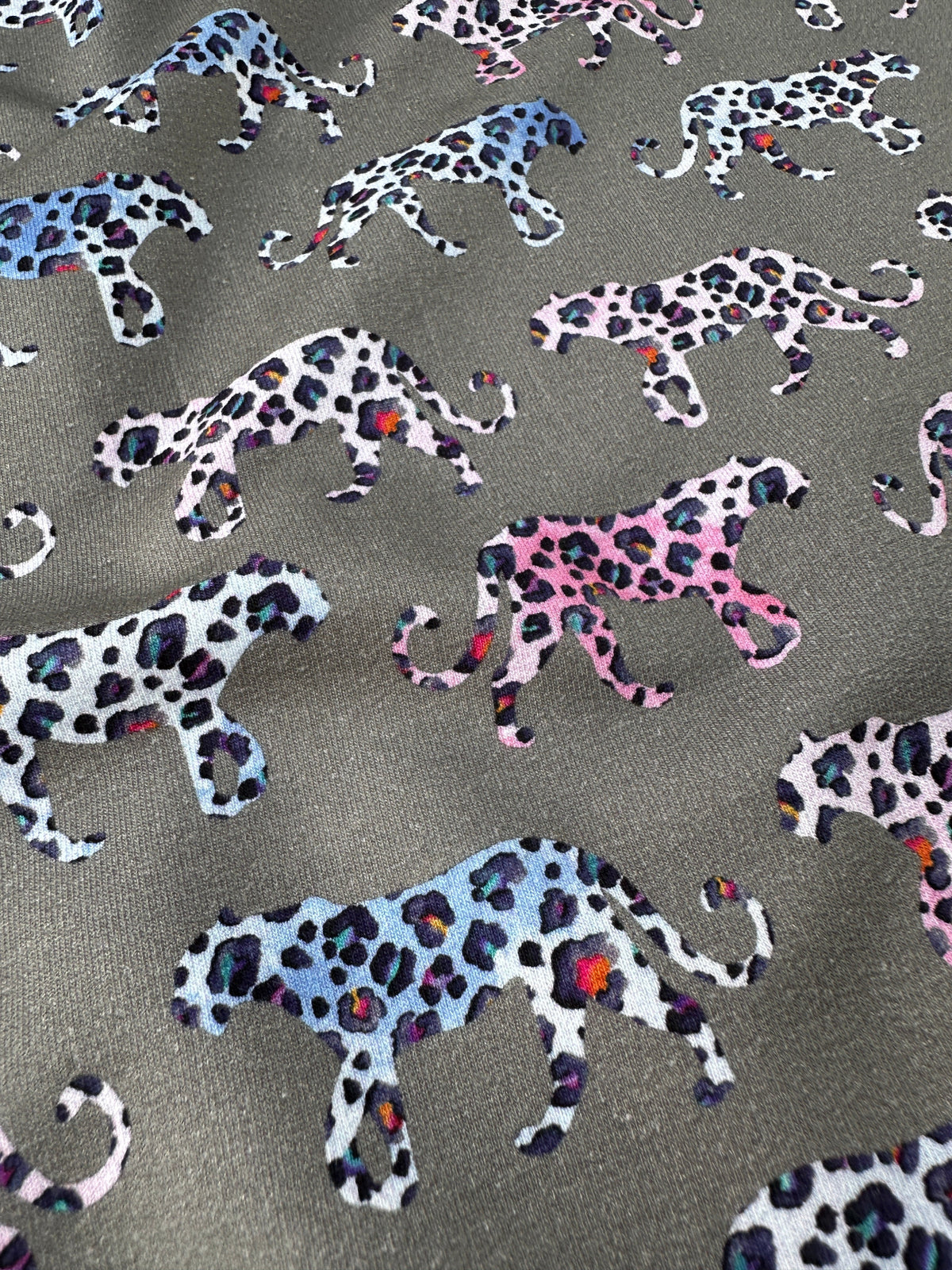 A close-up of fabric featuring a repeating pattern of walking leopard silhouettes in pink and blue on a grey background.