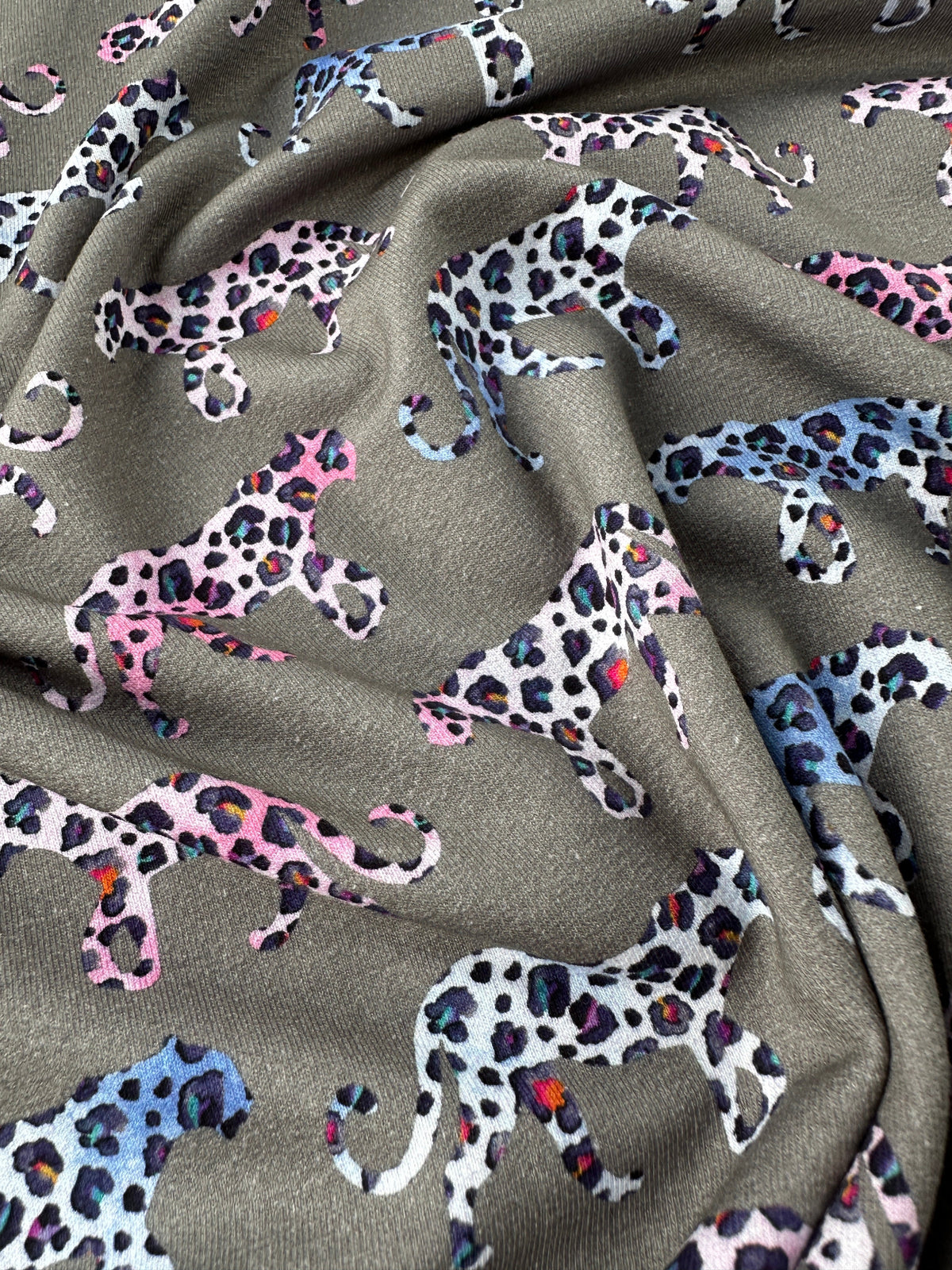 A close-up of draped fabric featuring an allover print of stylised leopard silhouettes in pink, blue, white, and black on a grey background.