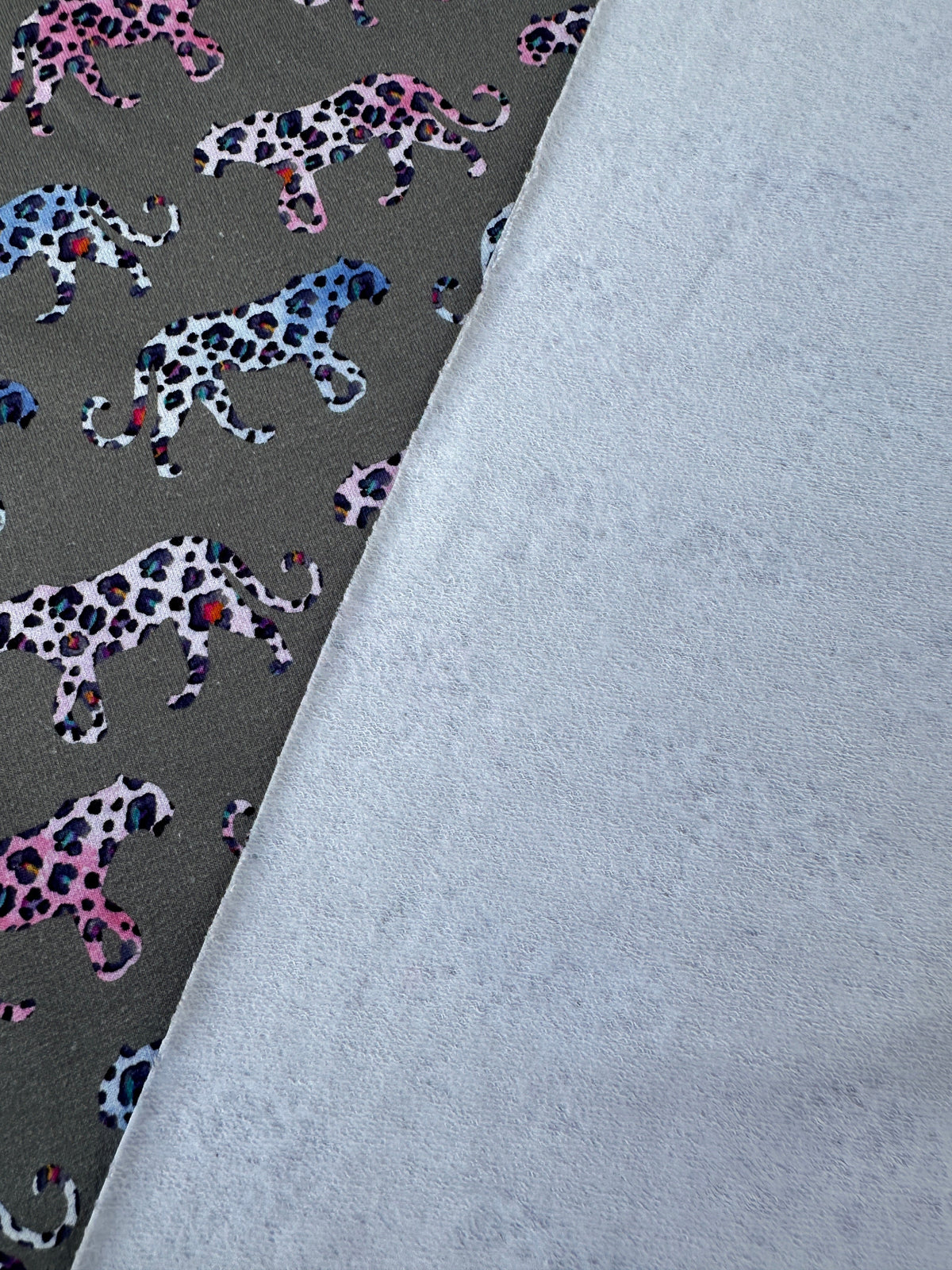 A close-up of the brushed back side of this fabric against the right side with colourful leopards on a grey background
