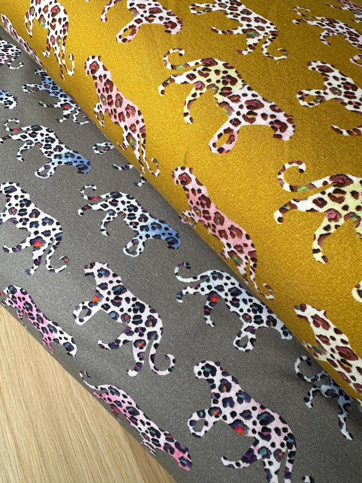 Two bolts of french terry fabric in grey and mustard with colourful leopards walking across them